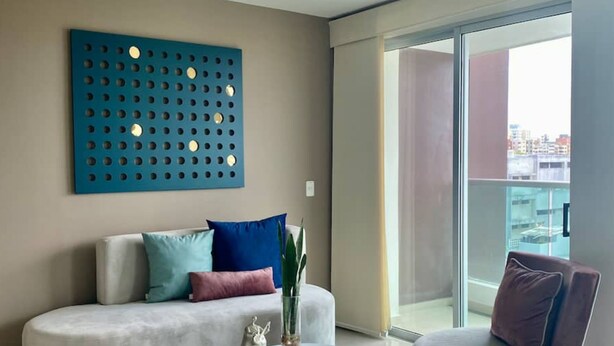 Una sala de estar moderna con un sofá, dos sillones, una mesa de centro y un panel decorativo en la pared.