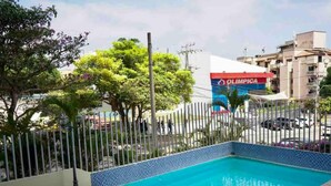 Una piscina con borde de azulejos, rodeada de una cerca y vegetación.