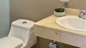 Un baño con inodoro, lavabo, espejo y una pequeña planta en maceta.