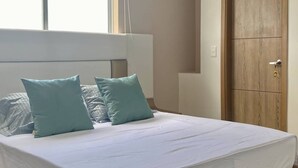 Un dormitorio con una cama, dos almohadas, una puerta de madera y un ventanal.