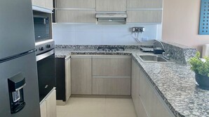 Una cocina compacta con horno empotrado, refrigerador de acero inoxidable, encimera de granito y un lavamanos pequeño.
