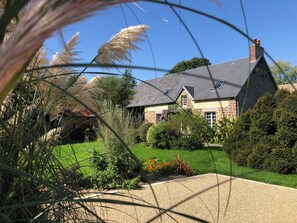 A stone house with a sloped roof, surrounded by a well-maintained garden and a gravel driveway.