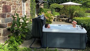 Una casa de piedra con jacuzzi en el patio trasero, rodeada de vegetación y una mesa de picnic.