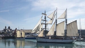 Un gran barco velero amarrado en un puerto con un edificio histórico al fondo.