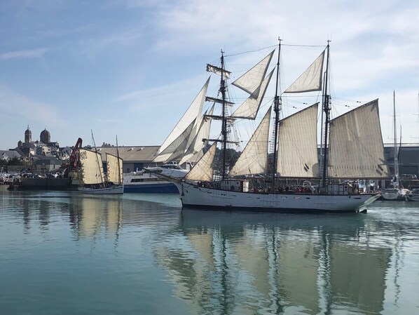 Um grande navio à vela atracado em um porto, com um edifício histórico ao fundo.