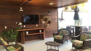 A cozy indoor seating area with wicker furniture, a flat-screen TV mounted on the wall, and potted plants. - Pousada Buriti (Conceicao da Barra)