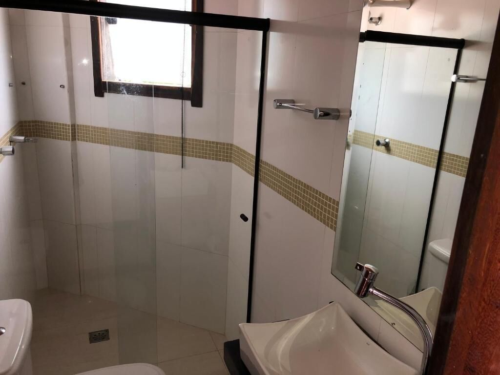 Casa de banho com cabine de chuveiro em vidro, pia e espelho.