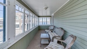 A covered porch with wicker furniture and large windows. - Riverview Townhouse II in Downtown Alexandria Bay (Alexandria Bay)