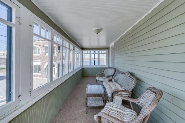 A covered porch with wicker furniture and large windows.
