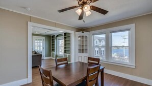 A dining area with a wooden table and chairs, a ceiling fan, and large windows with a view of the outside. - Riverview Townhouse II in Downtown Alexandria Bay (Alexandria Bay)