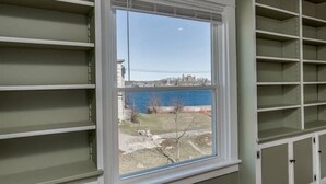 A room with a large window, white shelving units, and a view of a body of water and buildings. - Riverview Townhouse II in Downtown Alexandria Bay (Alexandria Bay)