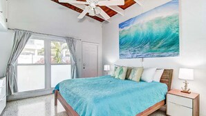 Ein Schlafzimmer mit einem großen Bett, einem Deckenventilator, einem Wellenbild und einem Fenster mit Vorhängen.