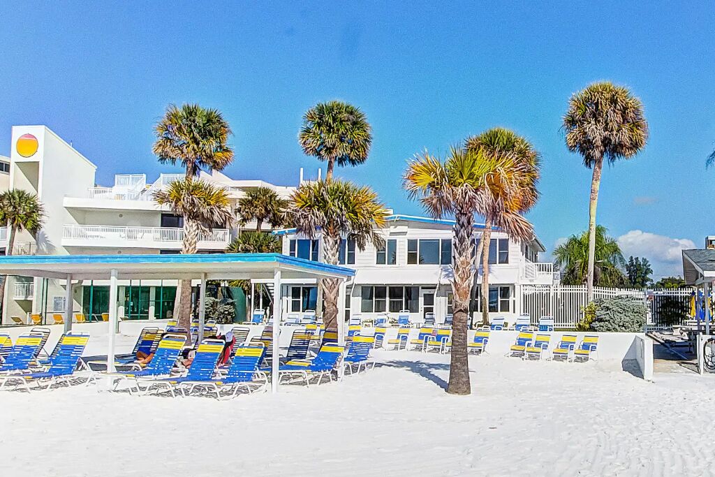 Ein Hotel am Strand mit mehreren Liegestühlen und Palmen.