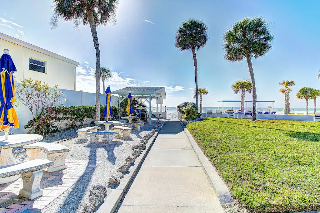 A pathway leading to a covered seating area with outdoor furniture and palm trees.