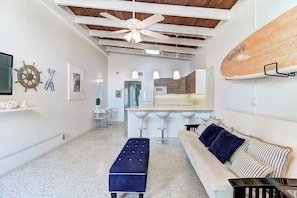 A modern living room with a white sofa, a blue ottoman, and a striped pillow. A wooden surfboard is mounted on the wall. - Beachfront Getaway in Siesta Key (Sarasota)