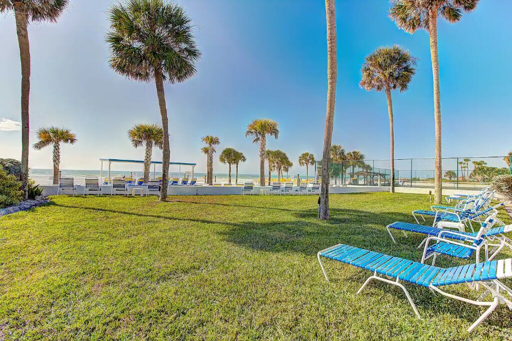 A beachside lounge area with rows of blue and white lounge chairs, palm trees, and a view of the ocean.
