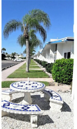 Relax in a serene outdoor space surrounded by lush greenery and a palm tree, with a mosaic seating area and pathway leading to a charming building.