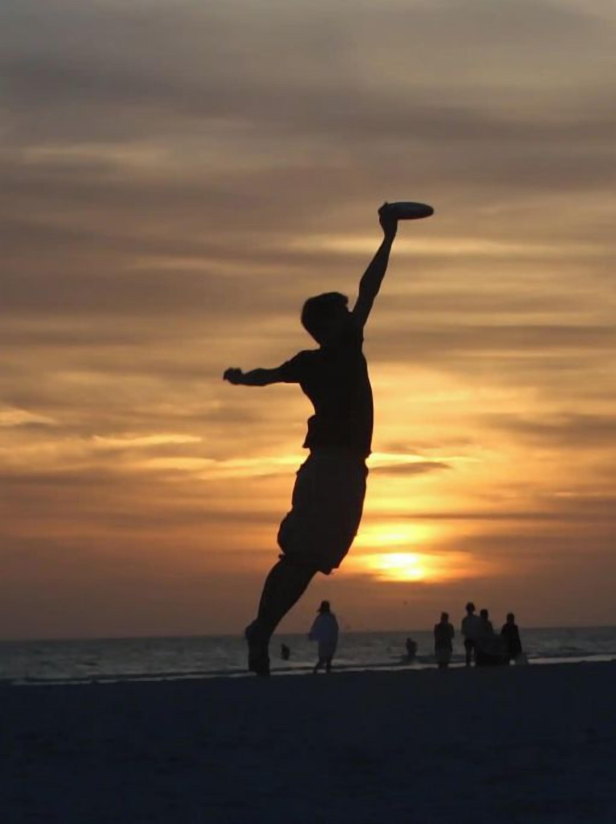 En siluett av en person som spelar frisbee vid solnedgången på en strand.