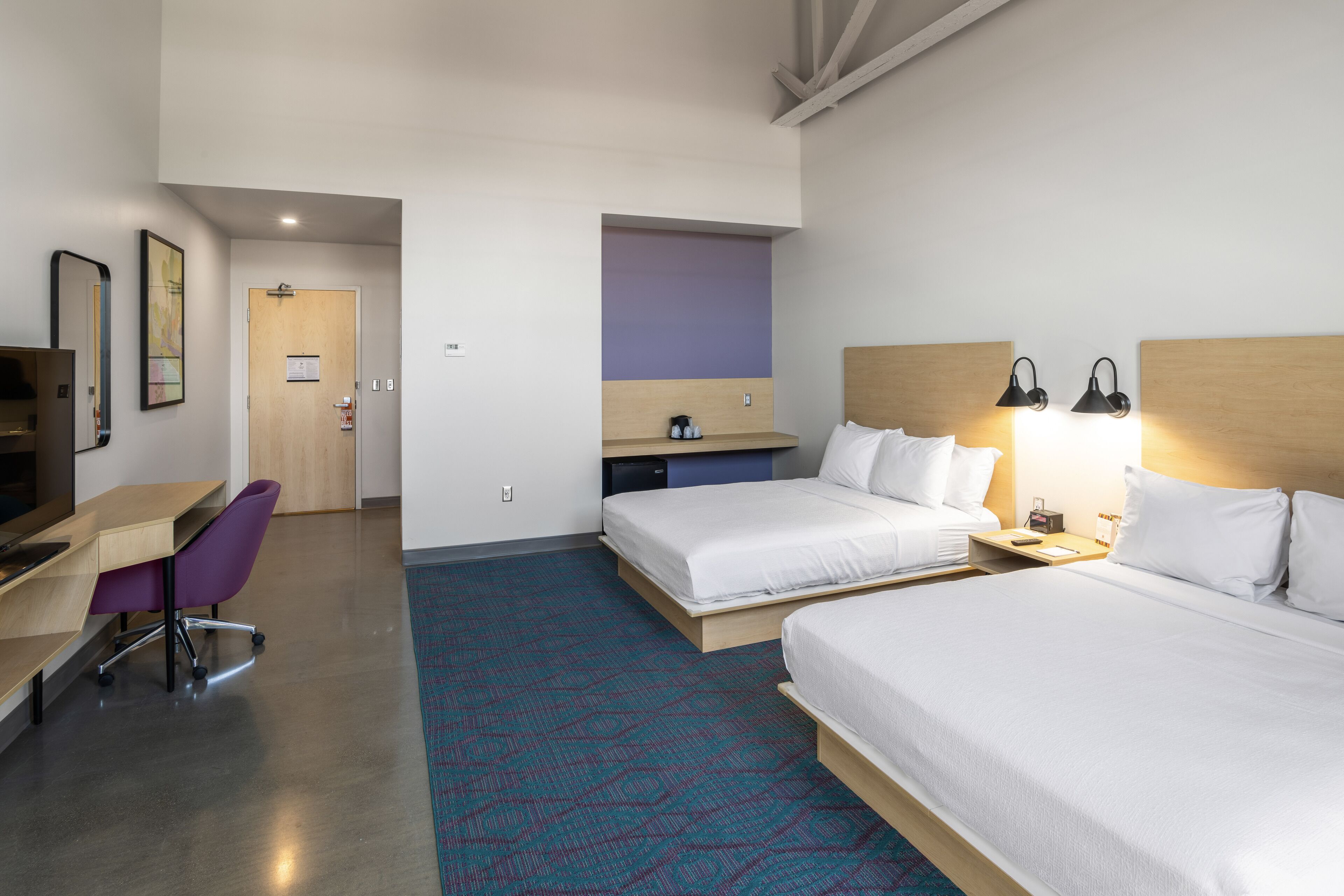 Ein Hotelzimmer mit zwei Betten, einem Schreibtisch, einem Sessel, einem Fernseher und einer Badezimmertür.