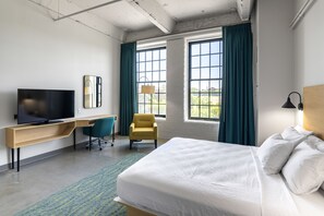 A hotel room with a bed, a desk with a TV, a chair, and large windows with curtains. - The Warehouse Hotel at Champion Mill (Hamilton)