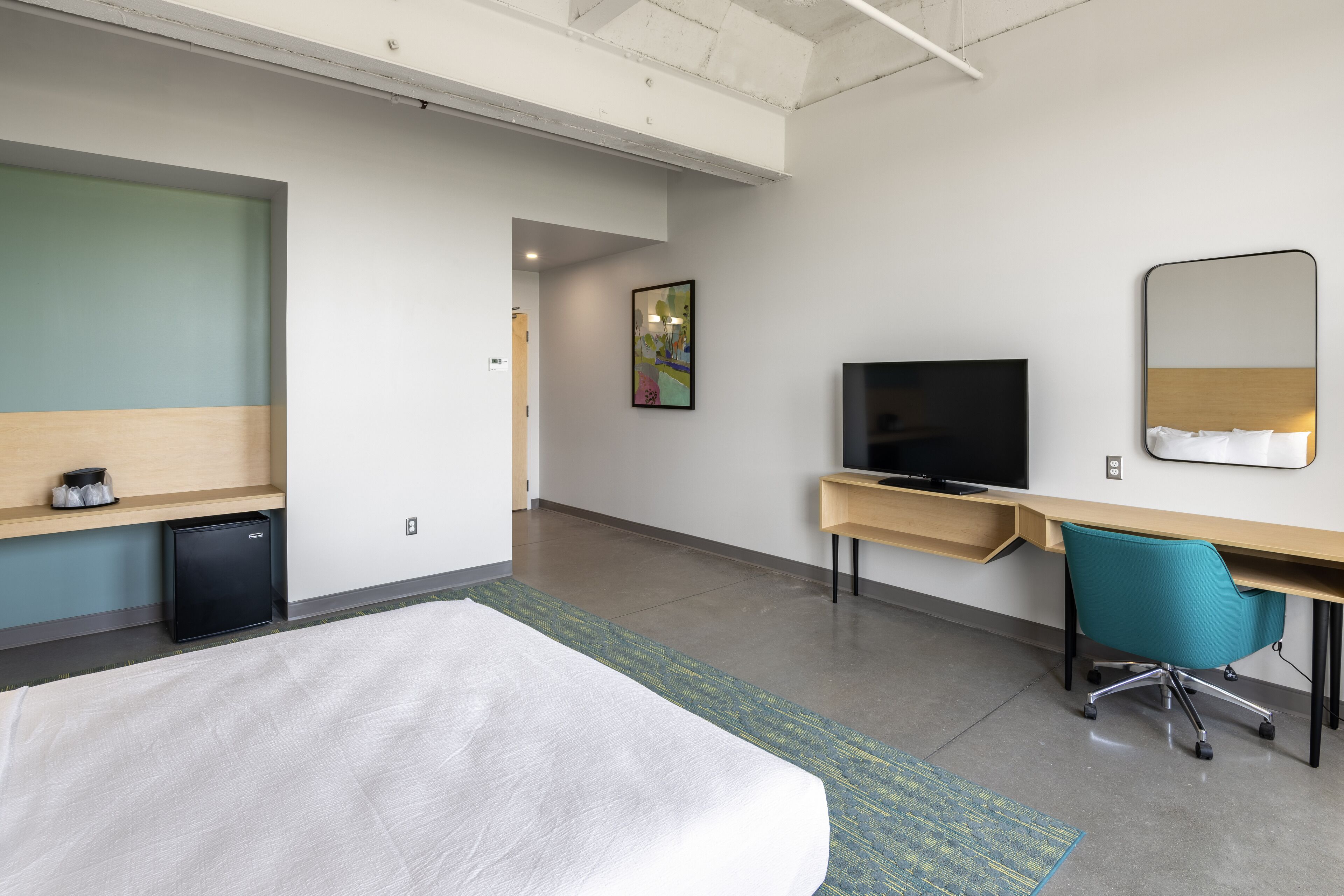 Une chambre d’hôtel comprenant un lit, un bureau avec une chaise, une télévision et un petit réfrigérateur.