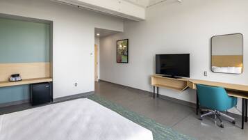 Une chambre d’hôtel comprenant un lit, un bureau avec une chaise, une télévision et un petit réfrigérateur.
