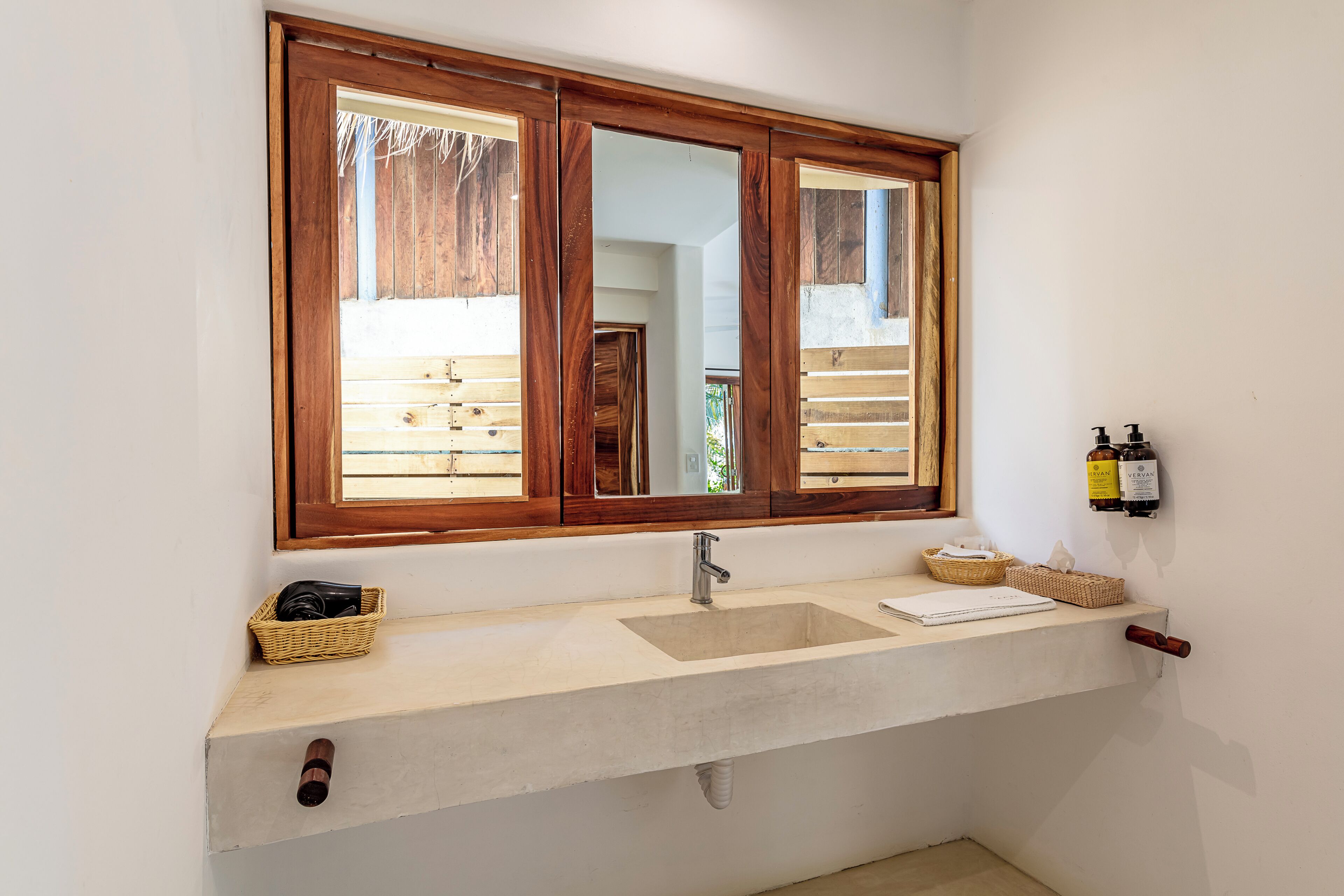 A bathroom with a wooden-framed window, a sink with a mirror, and a towel rack with bottles.