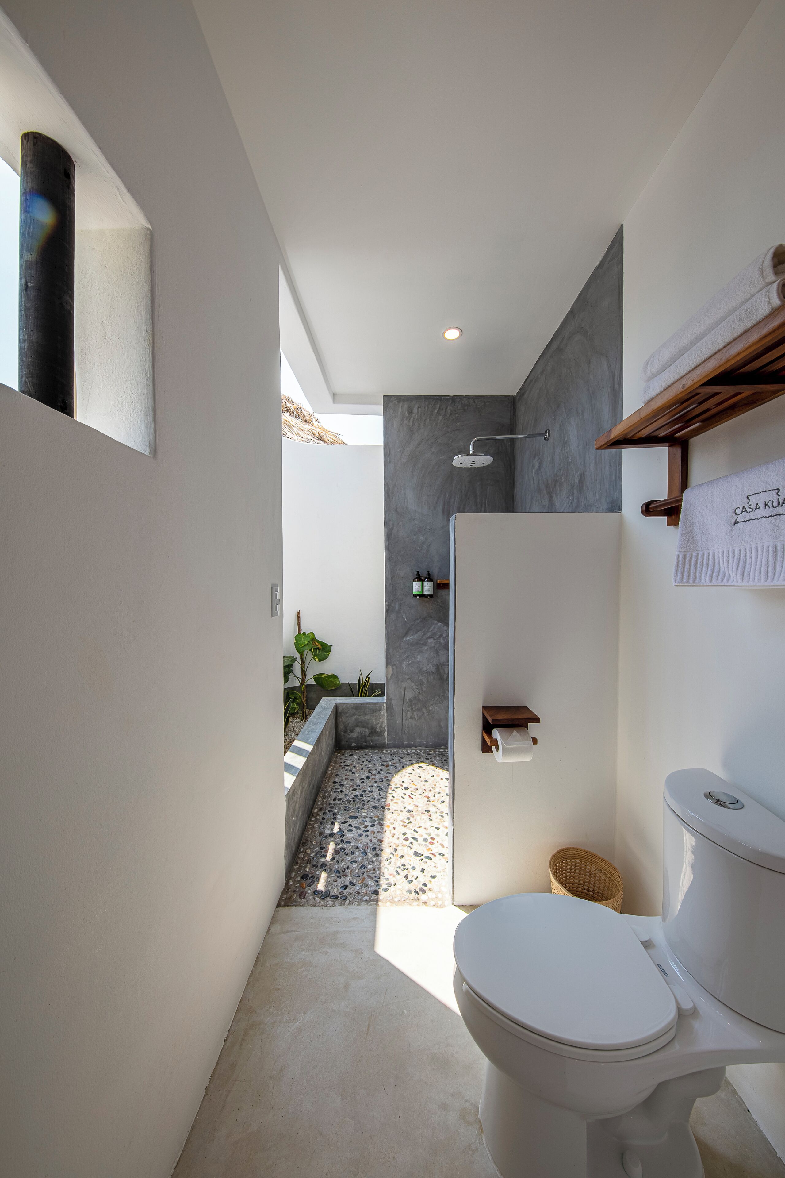 A modern bathroom with a white toilet, a shower, and a small sink. There is a towel rack with a towel hanging on it, and a basket on the floor.