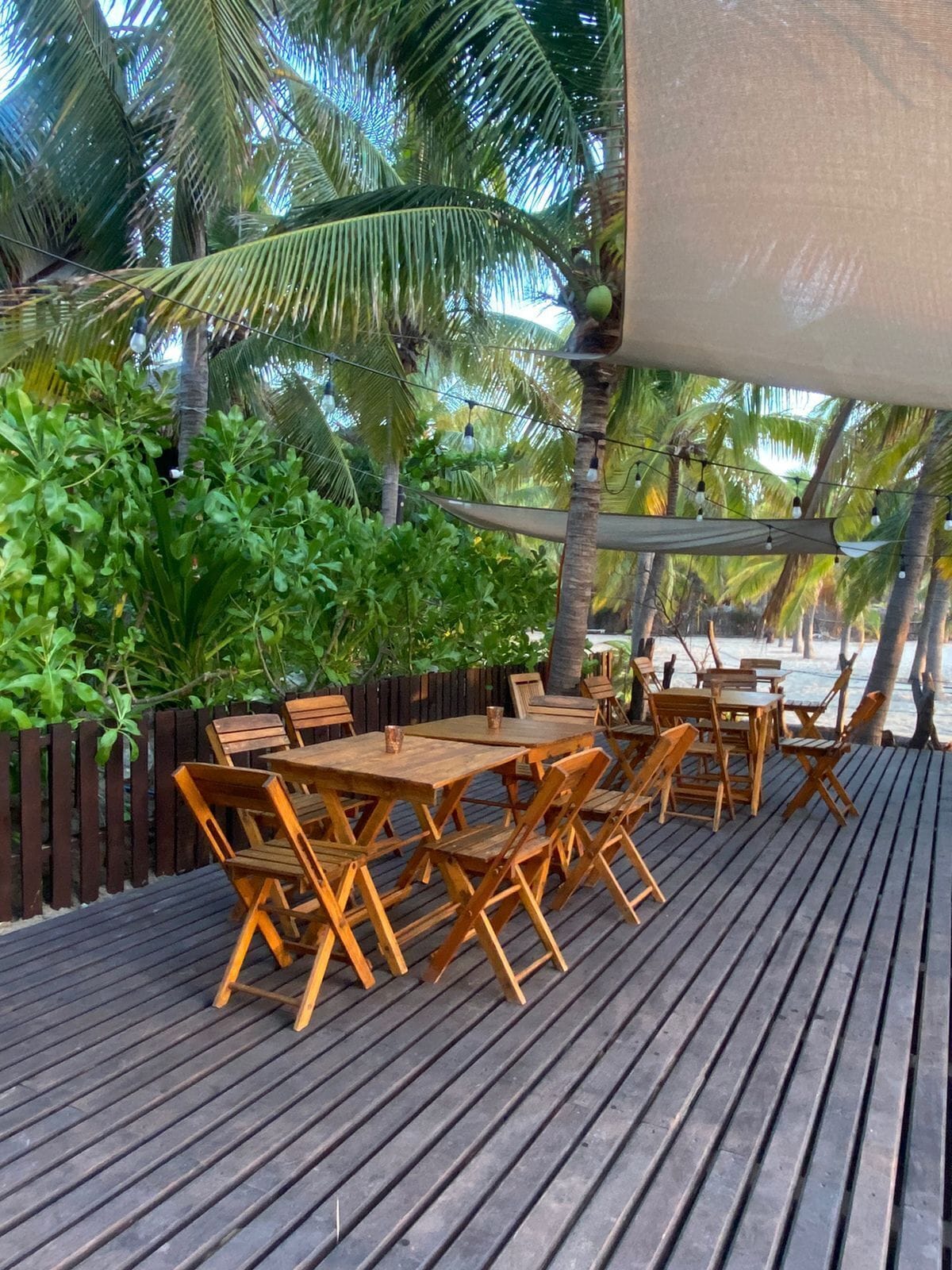 An outdoor wooden deck with tables and chairs, surrounded by lush greenery and palm trees.
