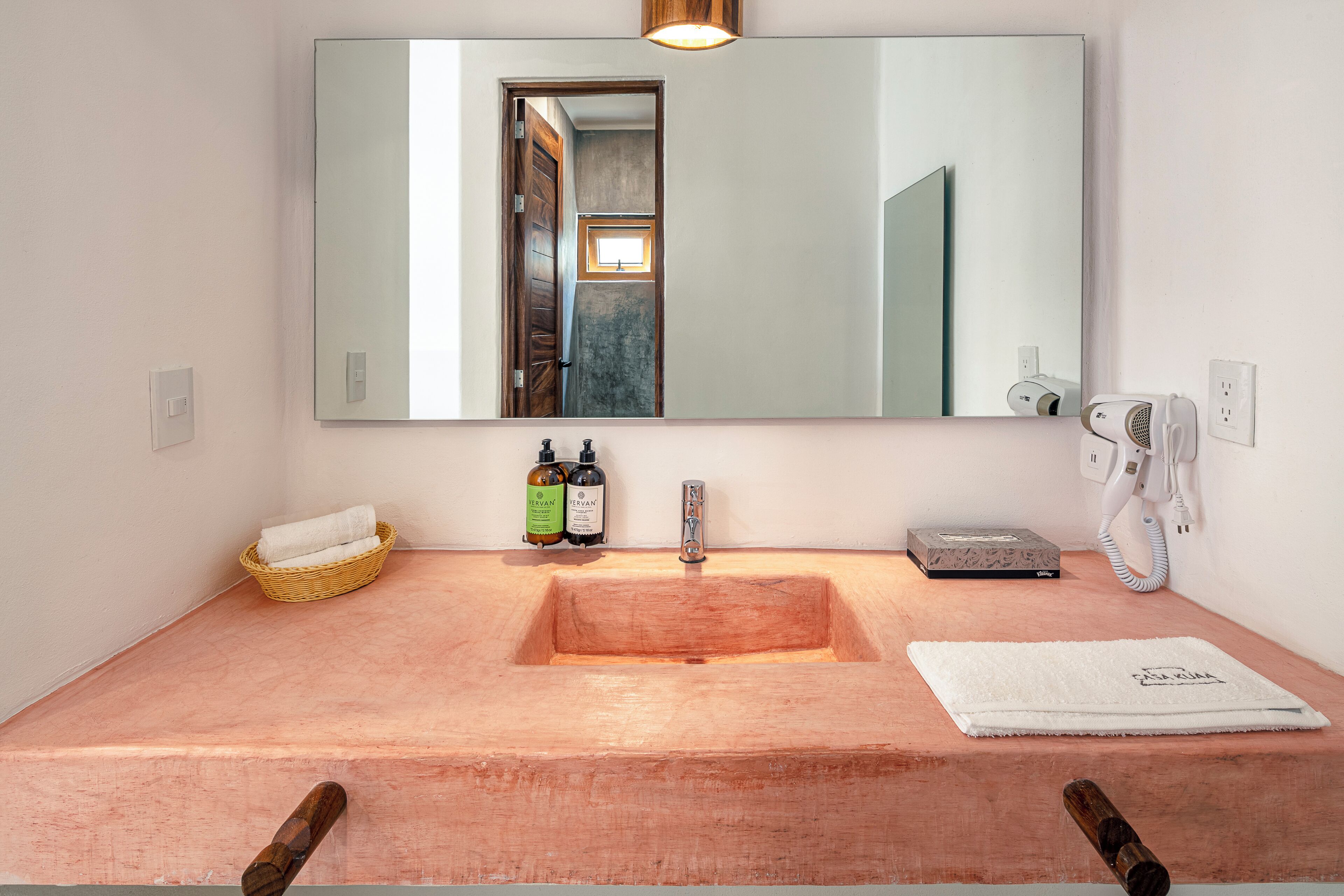 Un baño con tocador de madera, un espejo grande, una toalla y artículos de aseo.