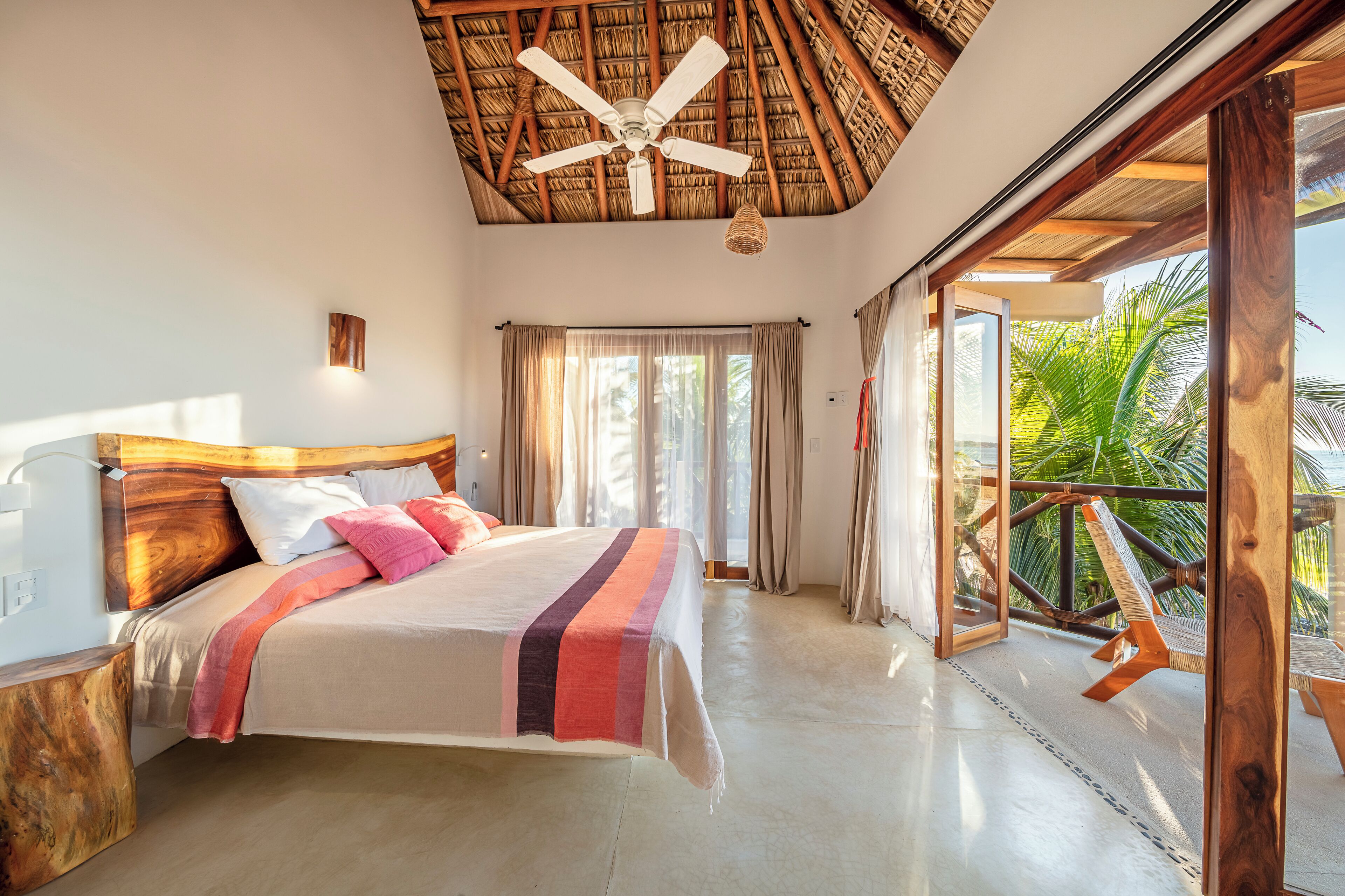 A bedroom with a bed, a ceiling fan, and a view of the outdoors.