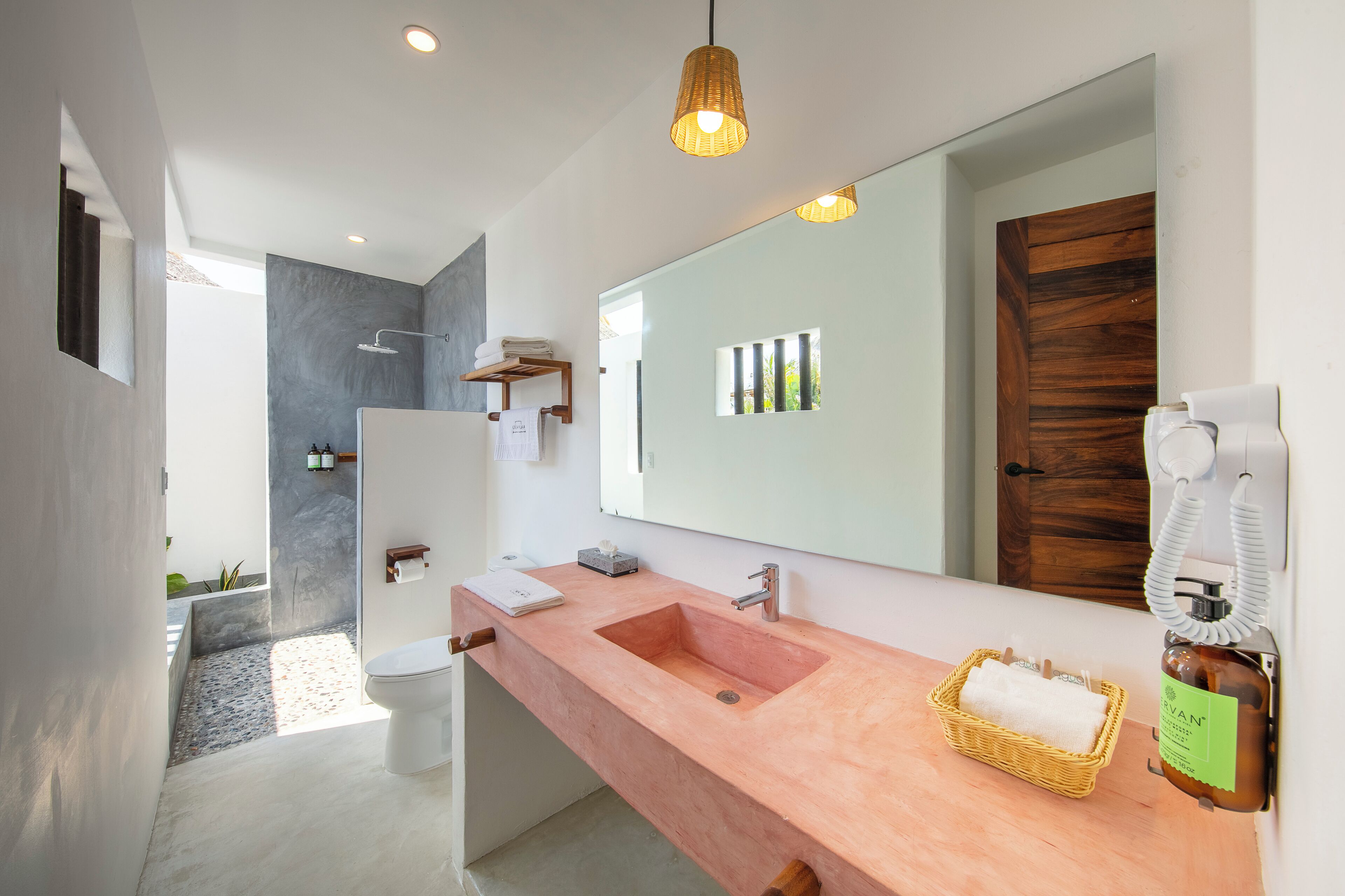 A modern bathroom with a large mirror, a pink sink, and a shower area.