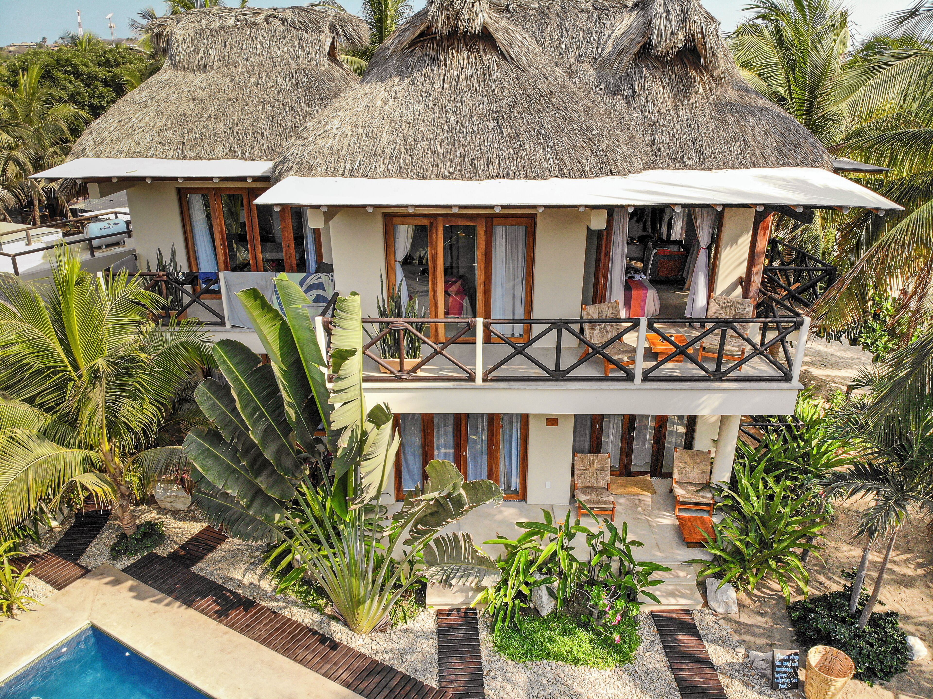 Un resort con piscina, edificios de techo de paja y plantas tropicales.