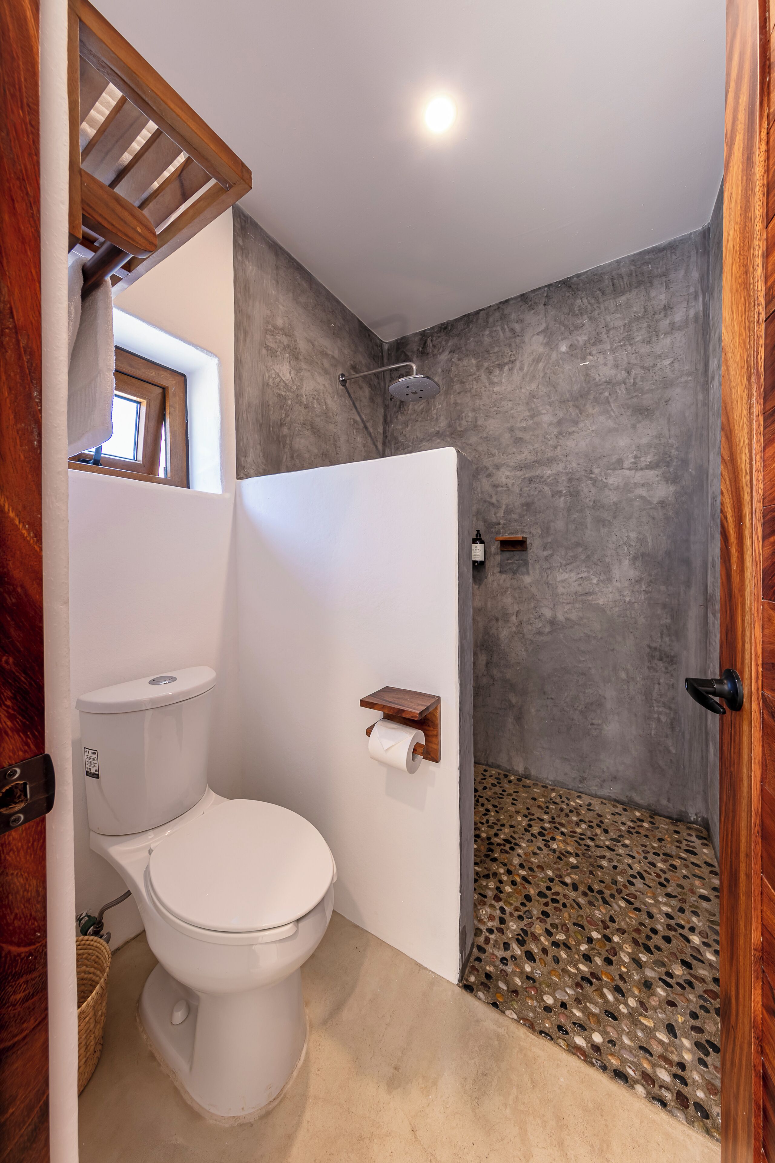 A bathroom with a toilet, shower, and a small window.