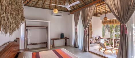 Une chambre spacieuse avec un grand lit, un ventilateur de plafond et une vue sur la terrasse extérieure.