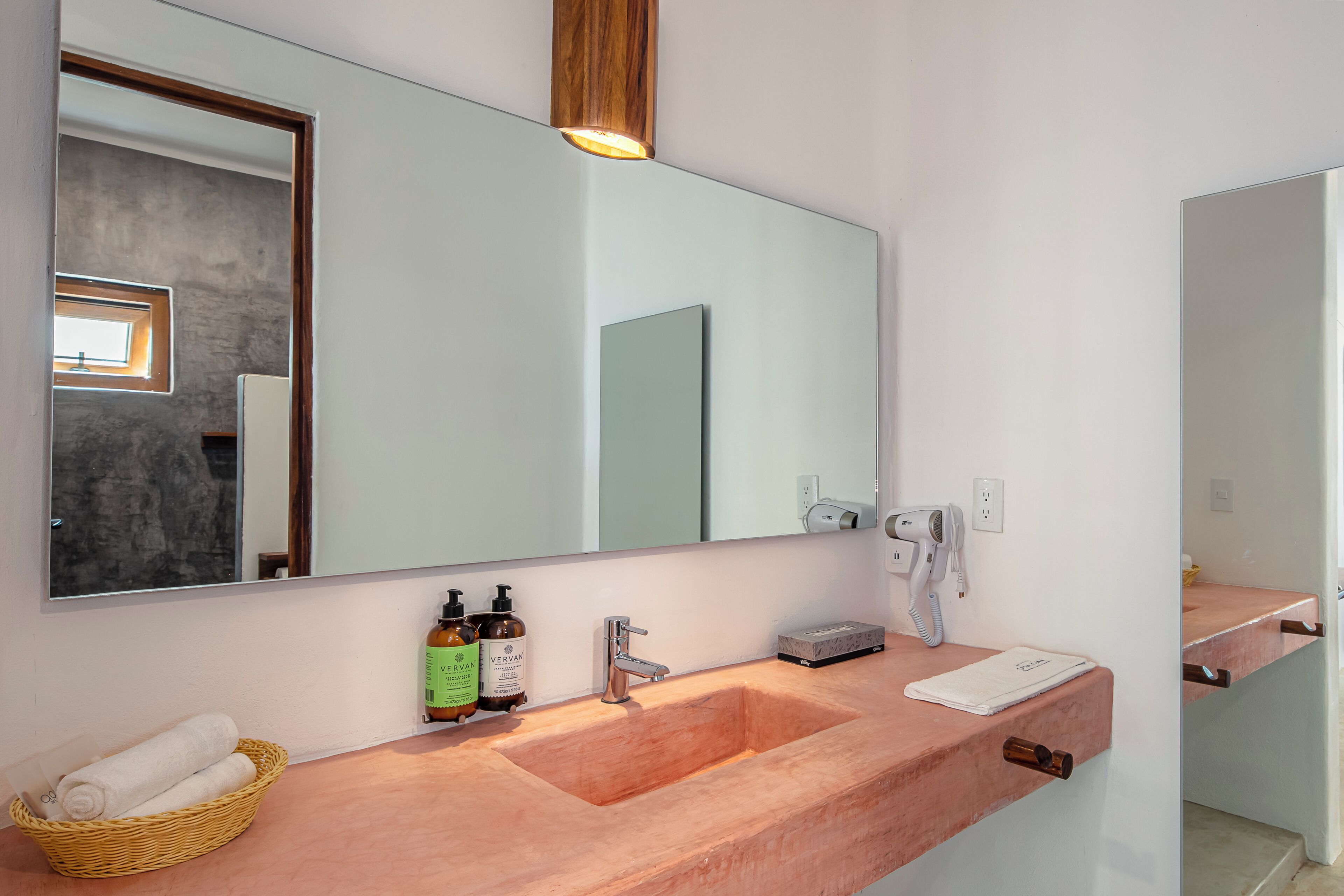 A modern bathroom with a large mirror, a wooden countertop, and a sink. There are two bottles of shampoo, a hairdryer, and a towel on the counter.