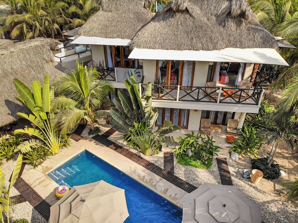 Un resort con piscina, edificios de techo de paja y exuberante vegetación tropical.