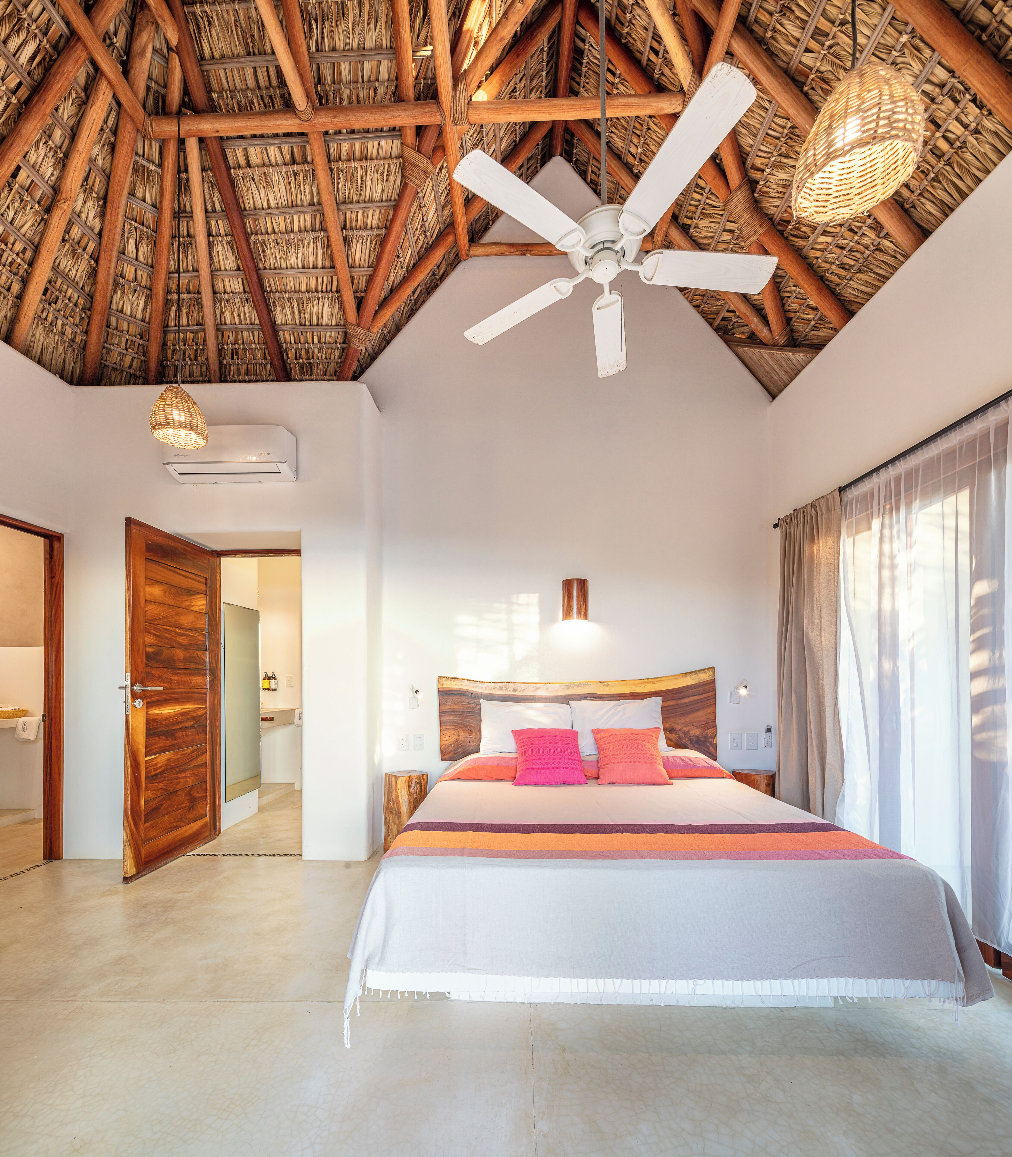 A spacious bedroom with a large bed, a ceiling fan, and a woven ceiling.