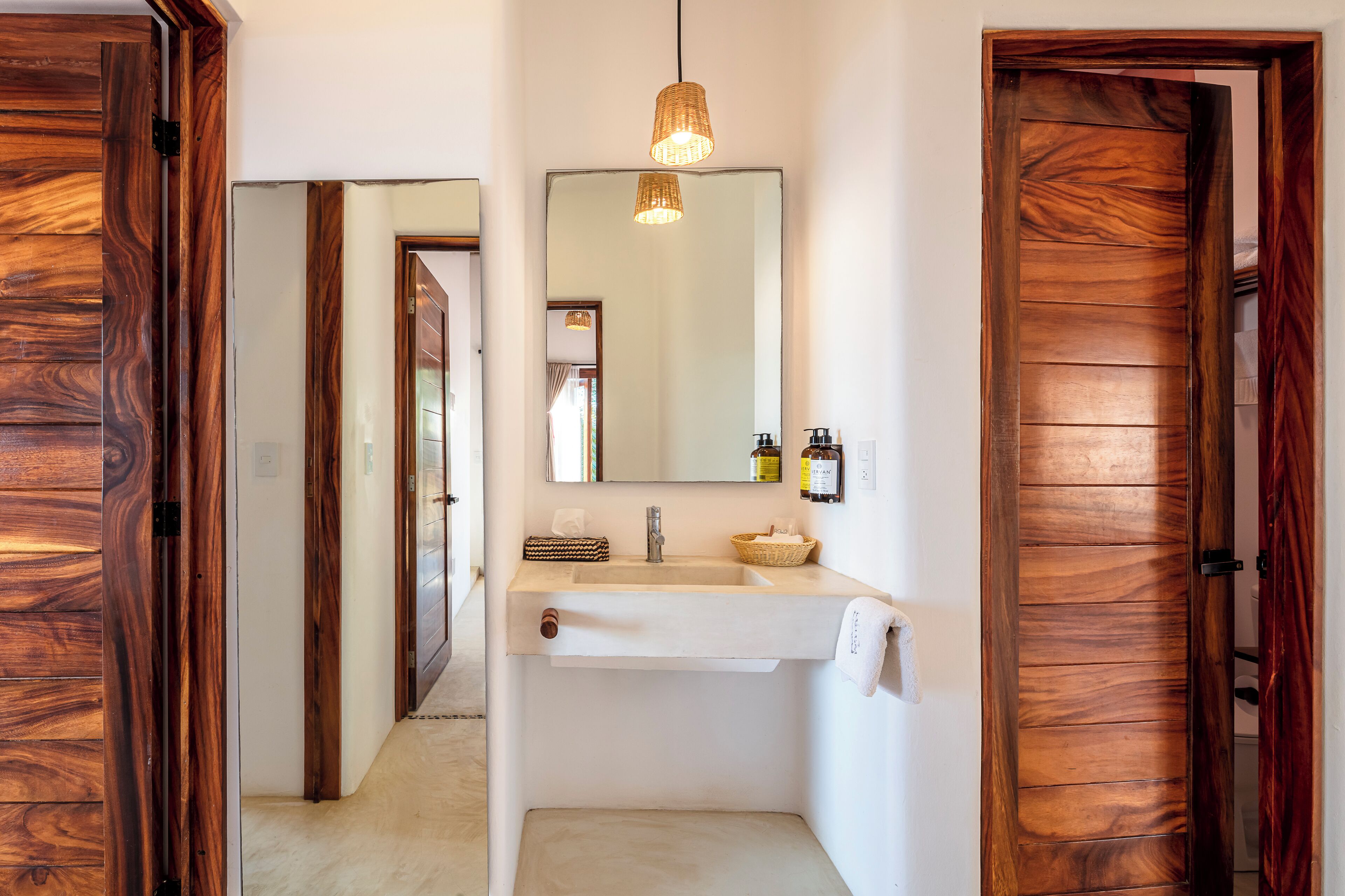 A bathroom with a wooden door, a white sink, a mirror, and a hanging light fixture.
