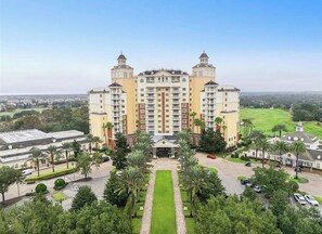A multi-story hotel with a central entrance, surrounded by a well-maintained lawn and palm trees.