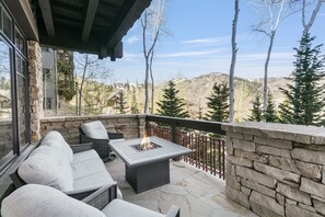 Une terrasse en pierre avec un foyer, des sièges d’extérieur et une vue sur un paysage montagneux.