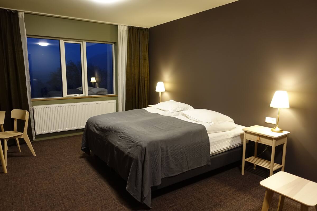 A hotel room with a bed, two bedside tables with lamps, a chair, and a window with curtains.