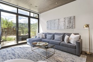 Relax in this stylish living room with a large sofa, coffee table, and floor lamp, offering a view of the surrounding mountains.