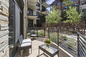 Enjoy the serene views from this outdoor balcony, featuring a glass table, wicker chairs, and a metal railing.