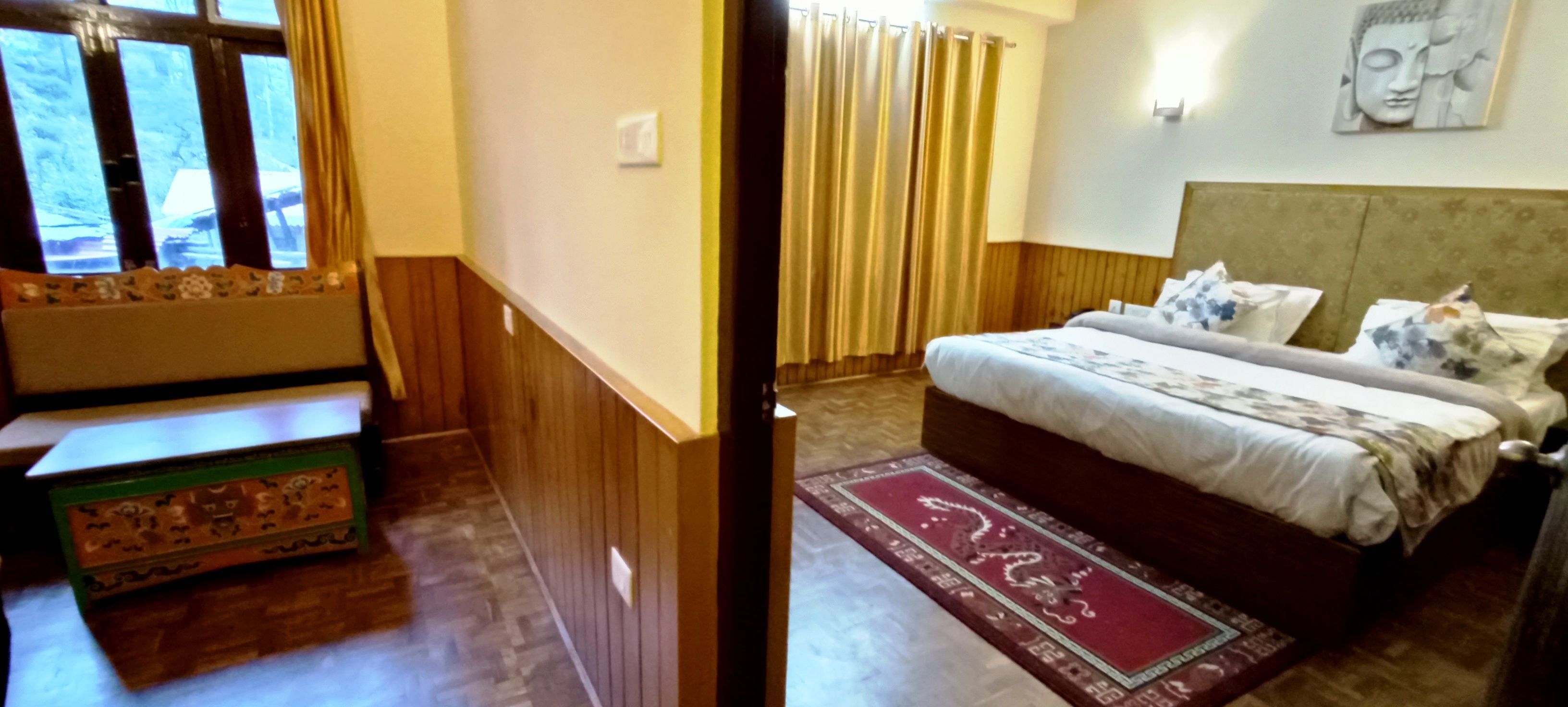 A hotel room with a bed, a wooden headboard, a nightstand, a window with curtains, and a wall-mounted light.