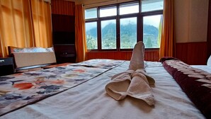 Una habitación de hotel con cama, escritorio, ventana y vistas a la montaña, además de cortina.