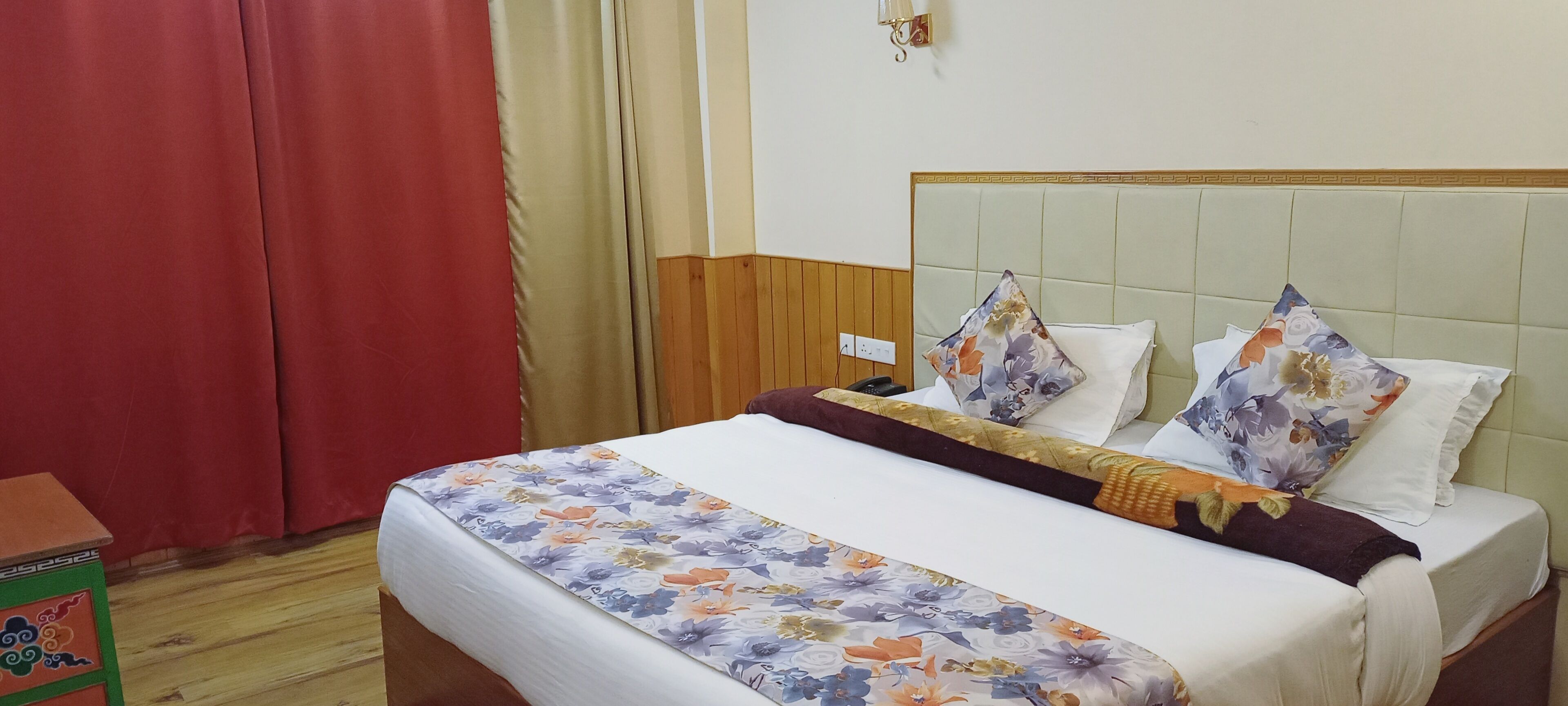 Een hotelkamer met een bed, gordijnen, een nachtkastje en een wandlamp.