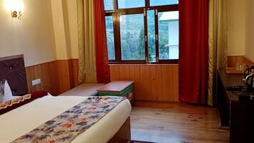 A hotel room with a bed, wooden panel walls, a window with curtains, a small table with a kettle, and a TV on a wooden stand.