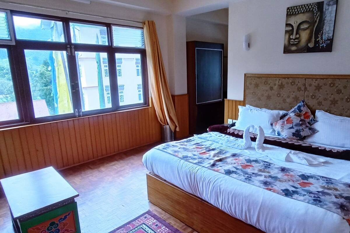 A hotel room with a large bed, wooden headboard, a Buddha painting, and a view through the window.