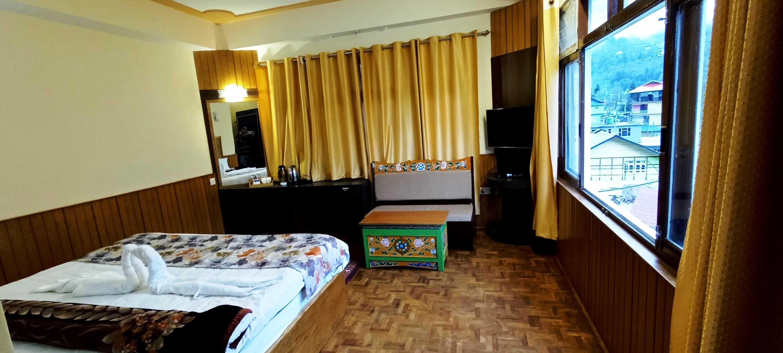 Ein Hotelzimmer mit Bett, einem kleinen Tisch, einem Spiegel, einem Fenster mit Vorhängen und Blick auf Gebäude.